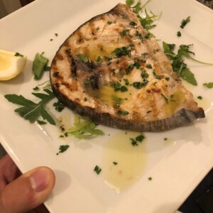 Spada grigliata con olio d'oliva e prezzemolo, servita su piatto bianco con limone e rucola, ottima presentazione culinaria napoletana