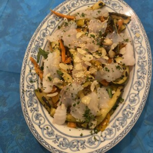 Piatto di pesce bianco a lamelle con verdure colorate, mandorle a lamelle e prezzemolo su piatto decorato blu, stile cucina napoletana, alimento fresco e leggero